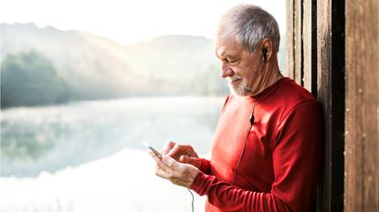 An older man smiles as he looks at his phone with mountains in the background.